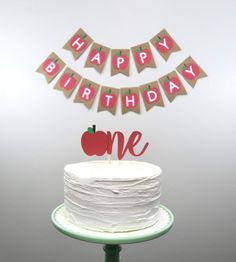 a white cake sitting on top of a wooden table next to a banner that says happy birthday one