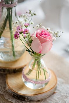 two vases filled with pink flowers on top of a wooden tablecloth covered table