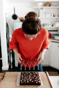 a woman cutting into a chocolate cake on top of a wooden table in a kitchen