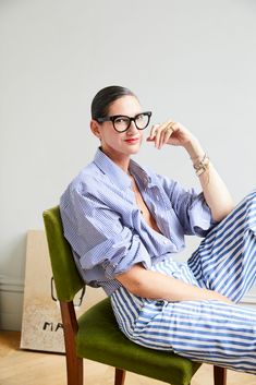 a woman sitting on top of a green chair with her legs crossed and wearing glasses