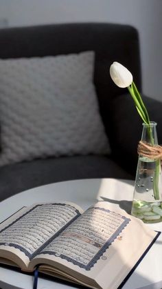 an open book on a table next to a vase with flowers in it and a candle