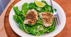 a white plate topped with meat and spinach covered in seasoning next to a fork