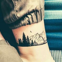 a person with a small tattoo on their arm that has trees and mountains in the background