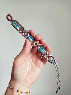 a hand holding a beaded bracelet in the shape of a long snake's tail