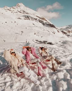 three women sitting in the snow with skis on their feet and one wearing sunglasses