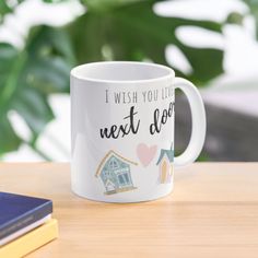 a white coffee mug sitting on top of a wooden table next to a book and plant