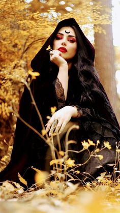 a woman with long black hair sitting in the woods