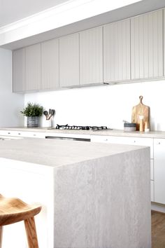 a kitchen with white cabinets and marble counter tops, along with a wooden bar stool