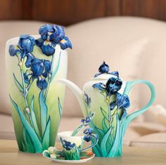 two vases with flowers painted on them sitting on a table next to a cup and saucer