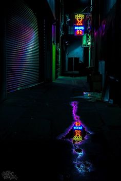 a dark alley with neon lights and a reflection on the wet ground in the water