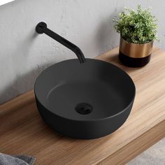 a round black sink sitting on top of a wooden counter next to a potted plant