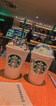 two starbucks drinks sitting on top of a wooden table