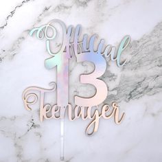 a cake topper with the number thirteen on it in pink and blue colors sitting on a marble surface