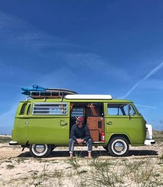 a man sitting in the back of a green van on top of a sandy beach