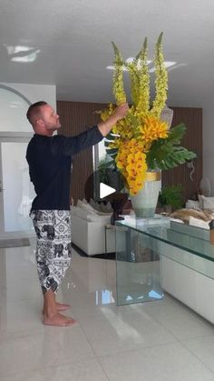 a man standing in front of a vase filled with yellow and white flowers on top of a table