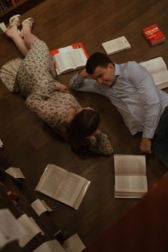 two people laying on the floor with books and papers scattered all over them, looking at each other