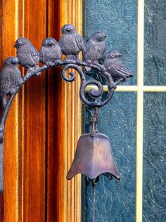 a metal bell with birds on it hanging from the side of a wall next to a window