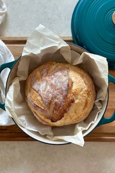 a loaf of bread sitting in a pot on top of a wooden table next to a blue pan