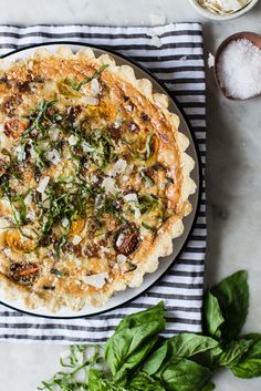 a pizza sitting on top of a white plate next to some green leaves and spices