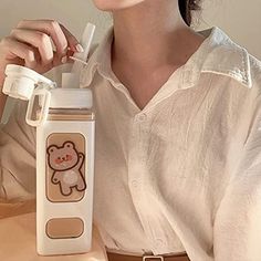 a woman sitting at a table with a bottle and cup in front of her face