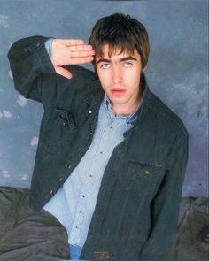 a young man in a denim jacket is holding his hand up to his ear and looking at the camera