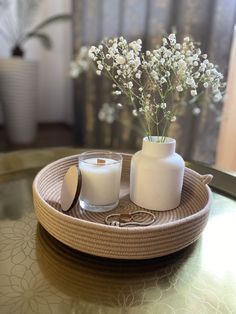 two white vases with flowers in them sitting on a tray next to a candle