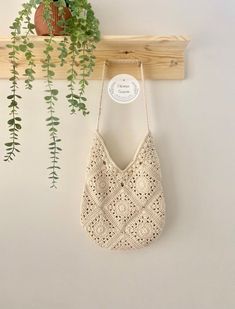 a crocheted bag hanging on a wooden shelf next to a potted plant