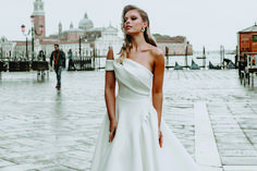 a woman in a white dress is standing on the street with her hands behind her back