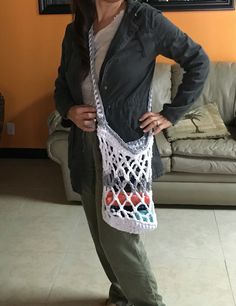 a woman standing in front of a couch holding a crocheted bag on her shoulder