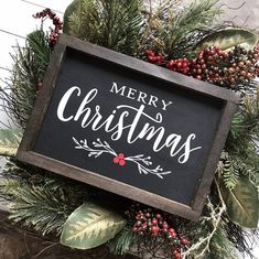 a merry christmas sign hanging on the side of a building with greenery and berries