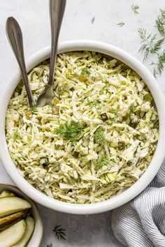 a white bowl filled with coleslaw and cucumbers next to two spoons