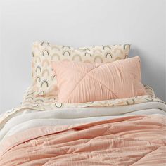 an unmade bed with peach colored sheets and pillows on top of it, next to a white wall