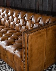 a brown leather couch sitting on top of a black and white rug next to a wooden wall