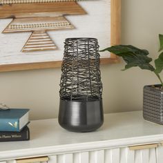 a black vase sitting on top of a white table next to a book and plant