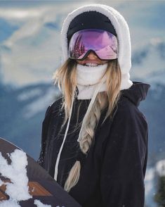 a woman holding a snowboard while wearing ski goggles