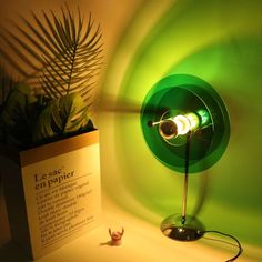 a green lamp sitting on top of a table next to a plant