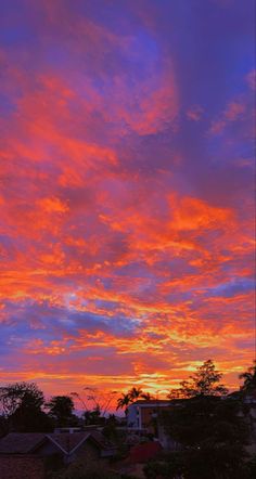 the sky is red and blue as it sets in the sunset over some houses with trees on either side