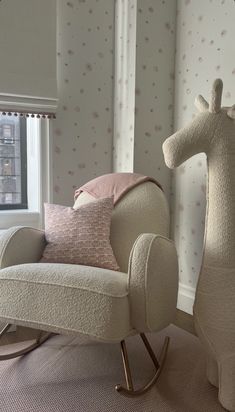 a rocking chair with a stuffed giraffe sitting on it's back in front of a window