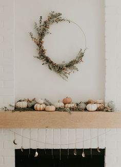 a fireplace with a wreath on top of it and pumpkins hanging from the mantel