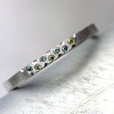 a silver ring with three different colored stones on it's side, sitting on a white surface