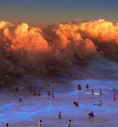 many people are in the water with surfboards and clouds behind them as they swim