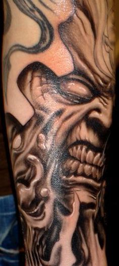 a man's arm with a black and grey tattoo design on it, featuring an evil face