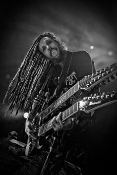 a man with dreadlocks on his face playing an electric guitar at a concert