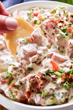 a hand dipping a tortilla chip into a white bowl filled with mexican chicken salad