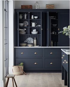 a kitchen with dark blue cabinets and white dishes on the counter top, along with a wooden stool