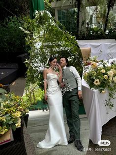 a man and woman standing next to each other in front of a table with flowers