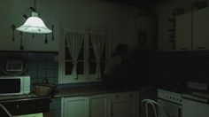 a man sitting on the counter in a dimly lit kitchen at night with his back turned to the camera