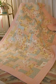 a bed with a pink and yellow quilt on it's side next to a window