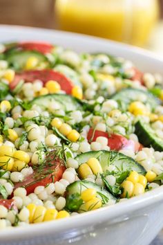 a salad with cucumbers, tomatoes, corn and herbs in a white bowl