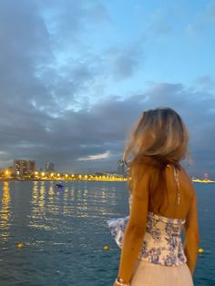 a woman standing on the edge of a boat looking out at the water and buildings in the distance